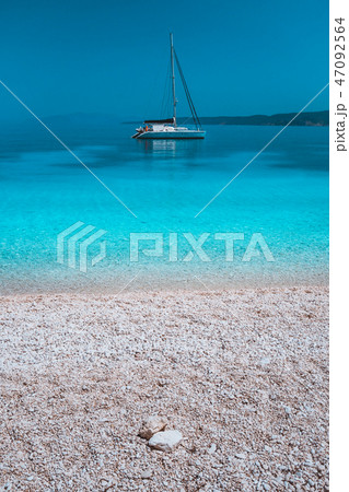 Pebble beach and white catamaran yacht boat in calm azure blue lagoon water at anchor 47092564