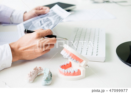 Concentrated dentist sitting at table with jaw samples tooth mod Concentrated dentist sitting at table with jaw samples tooth mod 47099977