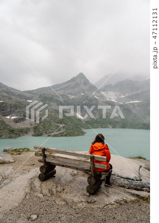 Young woman sitting on bench at mountain lake in the Alps Young woman sitting on bench at mountain lake in the Alps 47112131