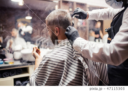 Hipster man client visiting haidresser and hairstylist in barber shop, smoking a pipe. Hipster man client visiting haidresser and hairstylist in barber shop, smoking a pipe. 47115303