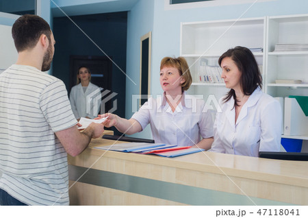 Qualified smiling doctors working with client at reception desk in hospital Qualified smiling doctors working with client at reception desk in hospital 47118041