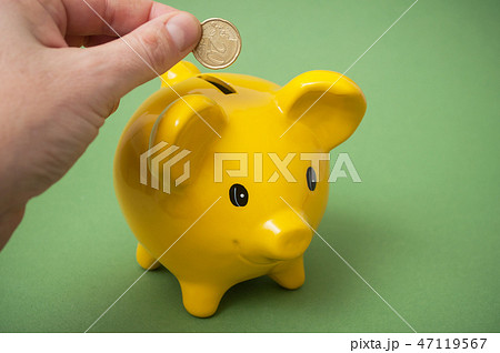 hand of man putting euro coin in yellow piggy bank 47119567