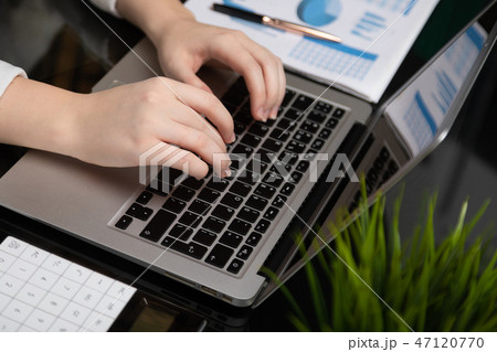 Close-up of female hands working on laptop analyzing graphs with calculator on glossy black table 47120770