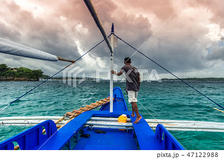 Young filipino man standing at edge of yacht looking at sea. Travelling on old boat at cloudy day. 47122988