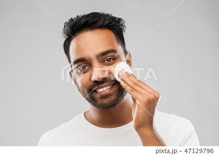smiling indian man cleaning face with cotton pad smiling indian man cleaning face with cotton pad 47129796