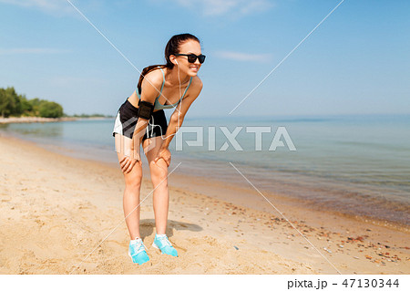 female runner with earphones and arm band on beach 47130344
