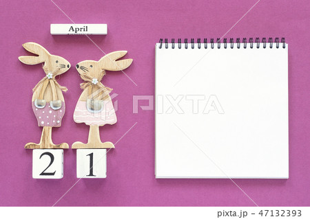 Calendar April 21 and pair of wooden easter bunnies, white notepad on purple paper background 47132393