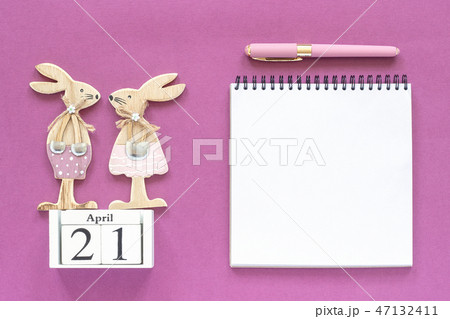 Calendar April 21 and pair of wooden easter bunnies, white notepad on purple paper background Calendar April 21 and pair of wooden easter bunnies, white notepad on purple paper background 47132411
