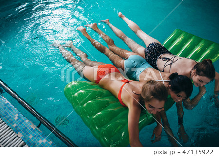 Three slim girlfriends wearing swimsuits lying on air mattress swimming in the swimming pool Three slim girlfriends wearing swimsuits lying on air mattress swimming in the swimming pool 47135922