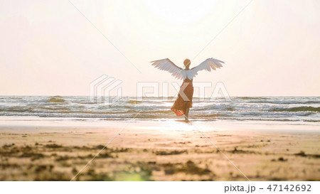 Beautiful female angel walking barefoot toward the sea at sunset. Beautiful female angel walking barefoot toward the sea at sunset. 47142692