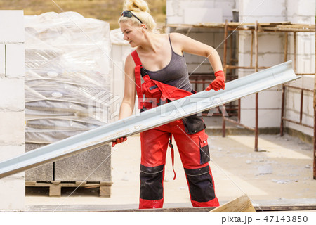 Woman carrying gutter on construction site Woman carrying gutter on construction site 47143850