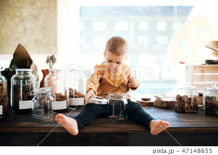 A barefoot small toddler boy sitting on a table in zero waste shop. A barefoot small toddler boy sitting on a table in zero waste shop. 47148655