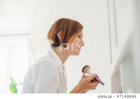 A young woman putting on a make-up in the morning in a bathroom. A young woman putting on a make-up in the morning in a bathroom. 47148684