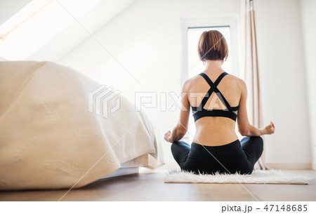 Rear view of young woman doing yoga exercise indoors in a bedroom. Copy space. Rear view of young woman doing yoga exercise indoors in a bedroom. Copy space. 47148685