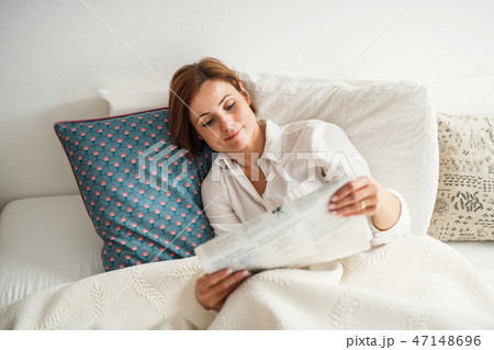 A young woman reading newspapers in bed in the morning in a bedroom. A young woman reading newspapers in bed in the morning in a bedroom. 47148696