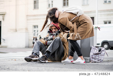 Young woman giving money to homeless beggar man sitting in city. Young woman giving money to homeless beggar man sitting in city. 47148824