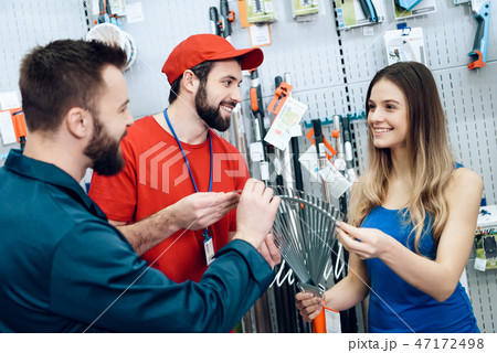 Two salesmen are showing female client new rake Two salesmen are showing female client new rake 47172498