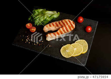 Grilled trout steak with a lemon and salad on a slate plate. 47175654