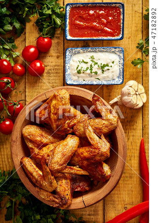 Delicious grilled chicken wings in bowl with spices and vegetables with dips on wooden table. 47182892