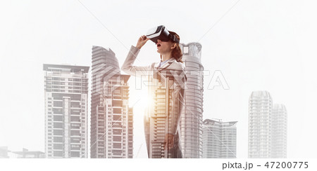 Woman in mask against sunrise above city trying virtual reality Woman in mask against sunrise above city trying virtual reality 47200775