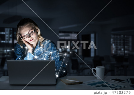 Attractive blonde wearing glasses in dark office using laptop. M Attractive blonde wearing glasses in dark office using laptop. M 47202279