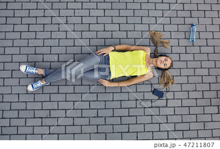 Young woman in a T-shirt with listening music and lies on the pavement 47211807