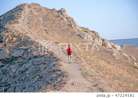 rear view of athletic runner running on a mountain trail on a blue sky background 47224581