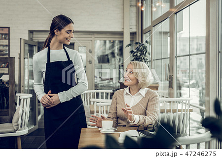 Smiling pleasant waitress speaking with her constant client Smiling pleasant waitress speaking with her constant client 47246275