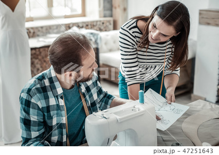 Bearded husband sitting at the sewing machine talking to wife Bearded husband sitting at the sewing machine talking to wife 47251643