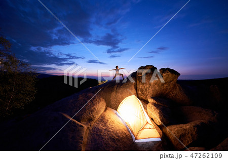 Camping on rock formation. Tourist tent and tourist girl doing gymnastic exercises on mountain top 47262109