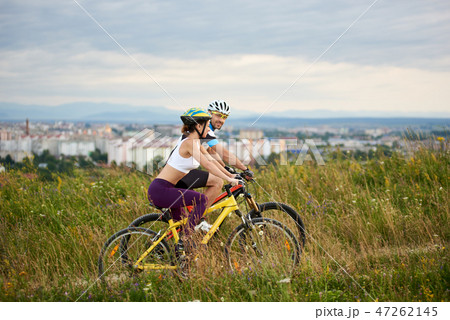 Two energetic cyclists in helmets riding bikes in high grass. Two energetic cyclists in helmets riding bikes in high grass. 47262145