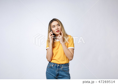 Portrait of a pensive young asian woman holding mobile phone and looking away thinking isolated over 47269514