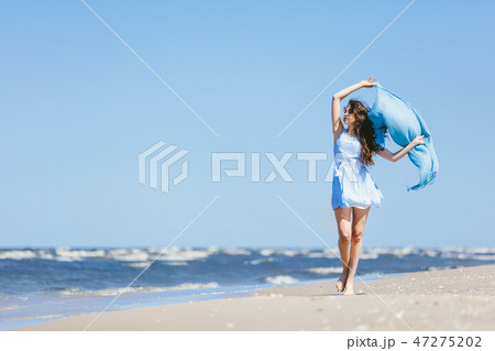 Young girl walking on the beach with blue scarf 47275202