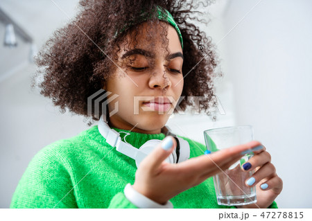 Serious curly girl having blue pill in palm and glass of water 47278815