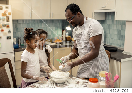 Caring father showing his daughters the way of beating eggs 47284707