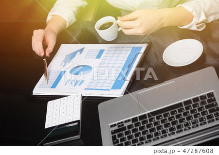 Businesswoman with coffee and pen points to graph 47287608