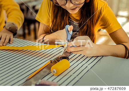 Red-haired girl wearing glasses cutting little yellow ribbon 47287609