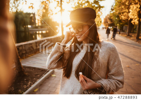Beautiful young girl listening to music in the park through a wireless earpiece Beautiful young girl listening to music in the park through a wireless earpiece 47288893
