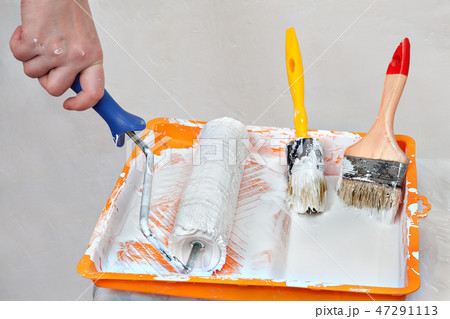 Hands painter dunks roller brush in tray of paint. Hands painter dunks roller brush in tray of paint. 47291113