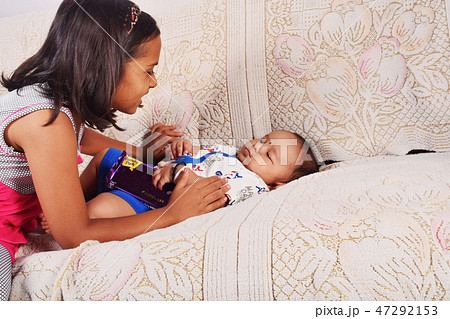 Sister playing with baby brother sleeping on sofa  47292153