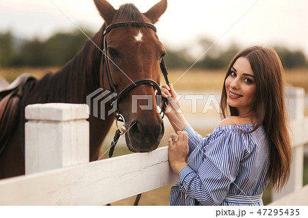 Beautiful pregnant woman stand near the horse. Lady in knitted hat and blue dress. Beautiful farm 47295435