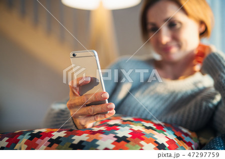 A young woman sitting indoors on a sofa at home, using smartphone. A young woman sitting indoors on a sofa at home, using smartphone. 47297759