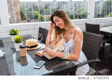 Beautiful girl sitting in city cafe in summer. Reads a paper book, next to a cup of coffee or tea Beautiful girl sitting in city cafe in summer. Reads a paper book, next to a cup of coffee or tea 47302545