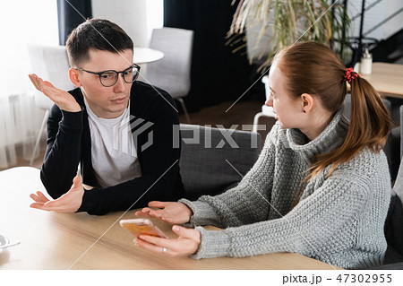 Girlfriend asking for explanation of her boyfriend sitting on a couch in the cafe Girlfriend asking for explanation of her boyfriend sitting on a couch in the cafe 47302955