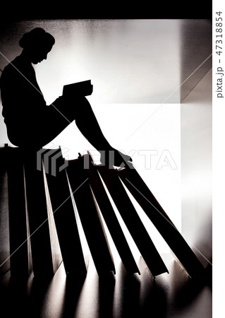 Silhouette of small woman on bookshelf reading book. 47318854