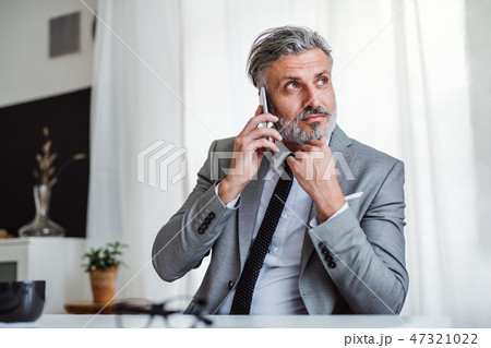 Serious mature businessman with smartphone sitting at the table, making a phone call. Serious mature businessman with smartphone sitting at the table, making a phone call. 47321022
