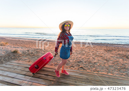 Travel, holiday and people concept - Happy laughing woman tourist standing near the sea with red 47323476