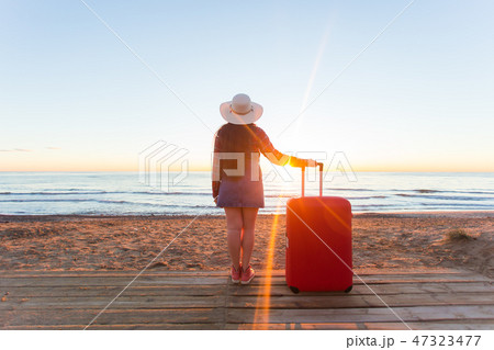 Holiday, travel and tourism concept - Beautiful women with red suitcase over sandy beach background 47323477