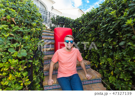 Holiday, travel and tourism concept - Handsome man with red suitcase sitting on a stairs Holiday, travel and tourism concept - Handsome man with red suitcase sitting on a stairs 47327139