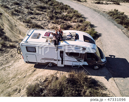 Couple sitting at motorhome roof waving hands 47331096